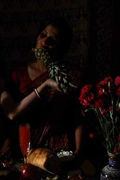 Amid flowers, fruits and juices, Tejal Shah and Marylea Madiman sit in Indian dress while Shah reclines as her partner force‑feeds her, creating an erotic tension that blurs sex and aggression. The scene intertwines seduction with repulsion and probes human condition, power, violence and identity.